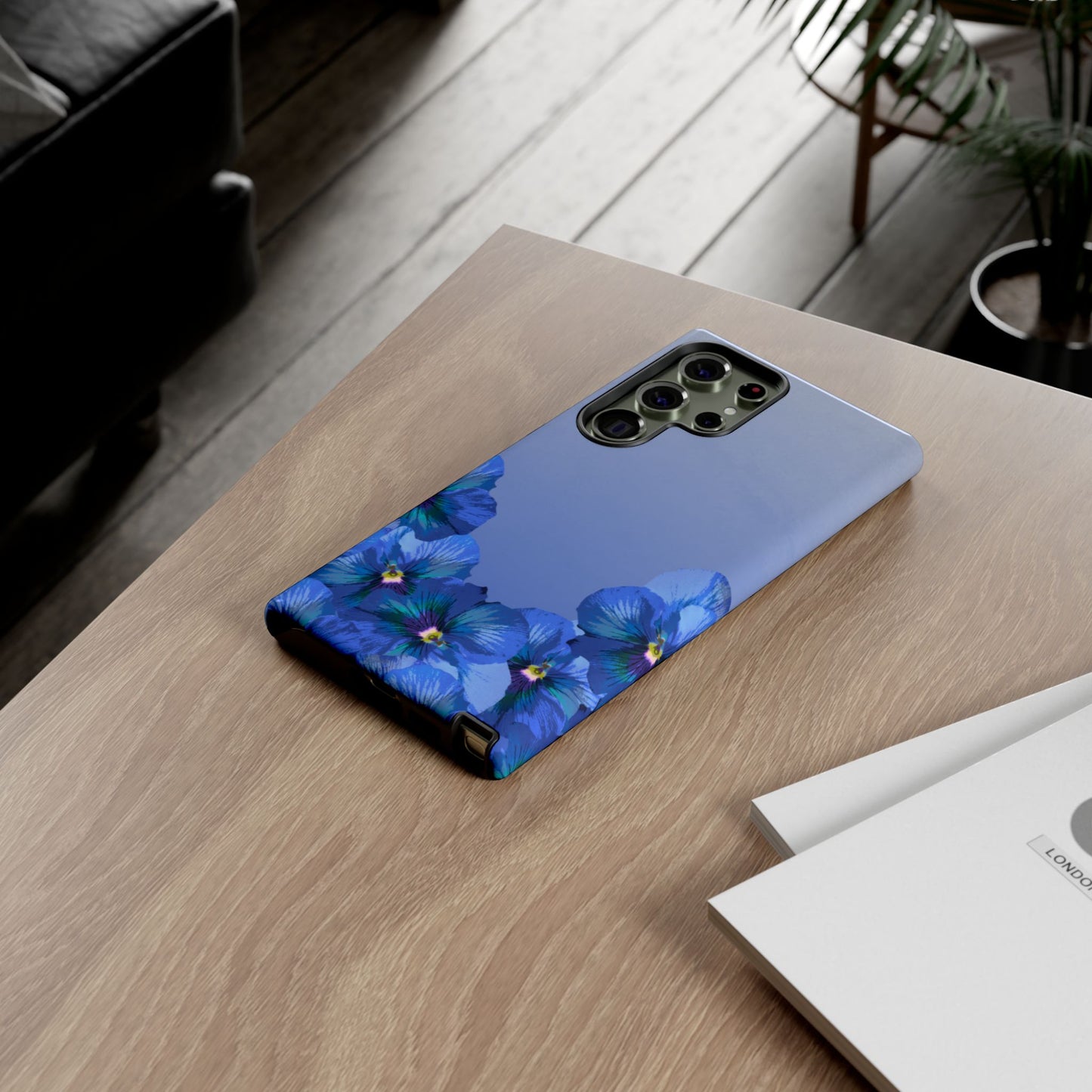 Blue pansy floral gradient Samsung Galaxy phone case shown on a wooden desk in lifestyle setting