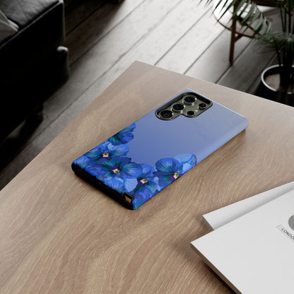 Blue pansy floral gradient Samsung Galaxy phone case shown on a wooden desk in lifestyle setting